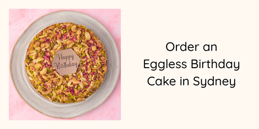 Eggless pistachio mawa birthday cake with happy birthday charm on pink background, Sydney online ordering guide hero image