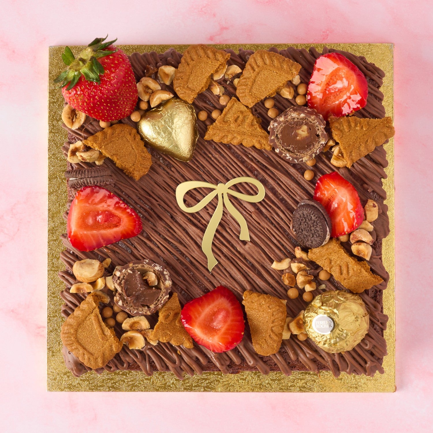 Christmas Brownie Cake in Sydney topped with strawberries, Biscoff, nuts, Ferrero Rocher and a golden bow charm