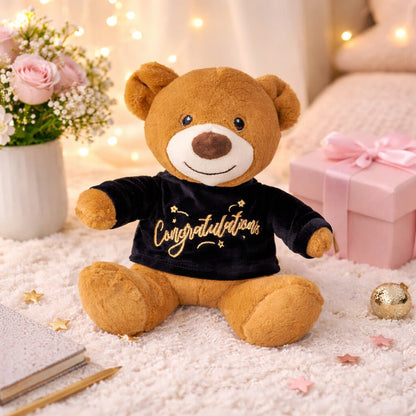 Plush congratulations teddy bear displayed as a gift add-on with celebration decor, suitable for hampers, desserts, and milestone gifting