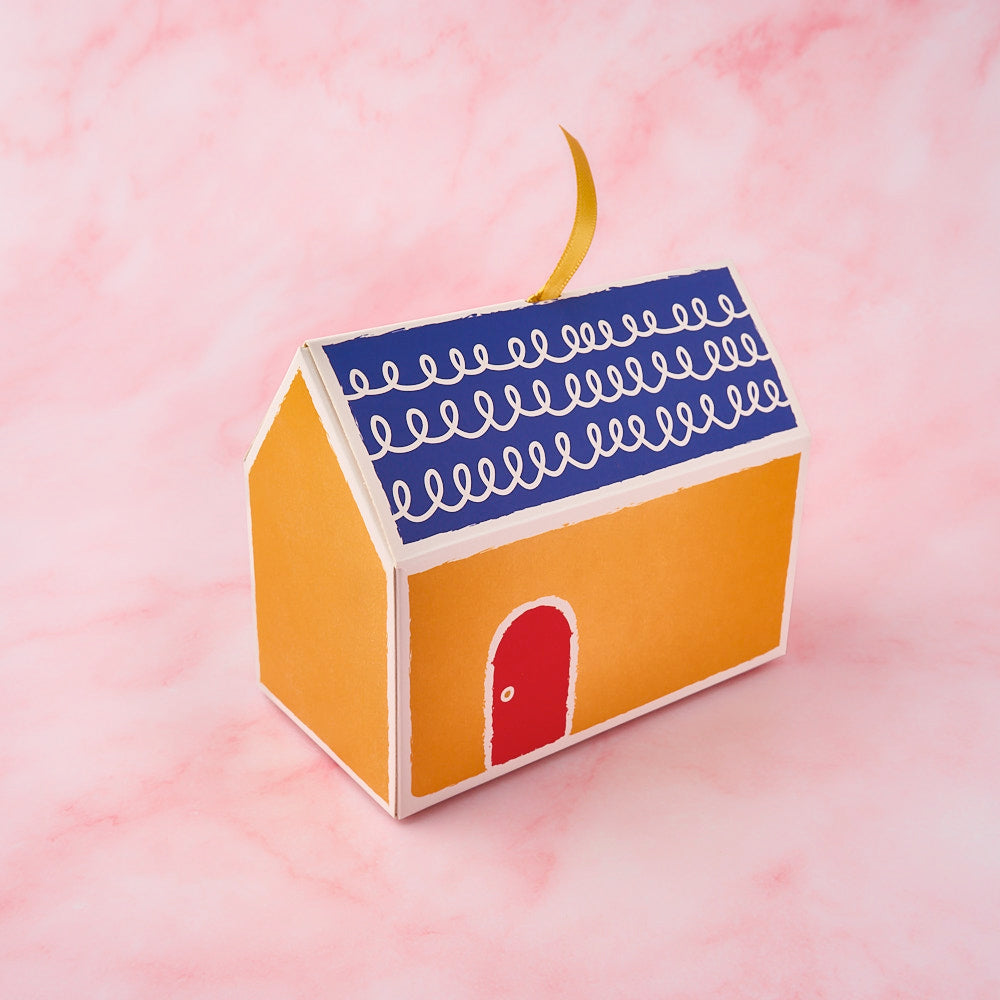 Grah Pravesh return gift box in a yellow house design with blue roof and red door by EatWithSimer