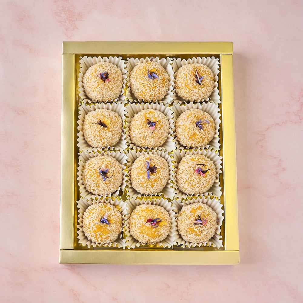 12 Mango Coconut Laddoos arranged in a gold-coloured tray in gift box