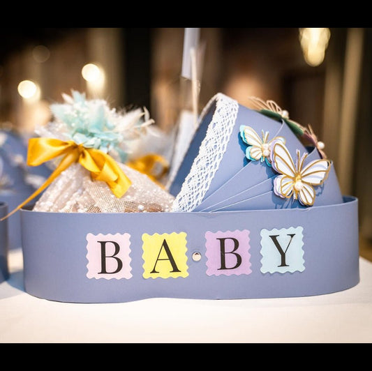 New baby bassinet gift hamper in blue basket with personalised card and eggless Pistachio Mawa Cake