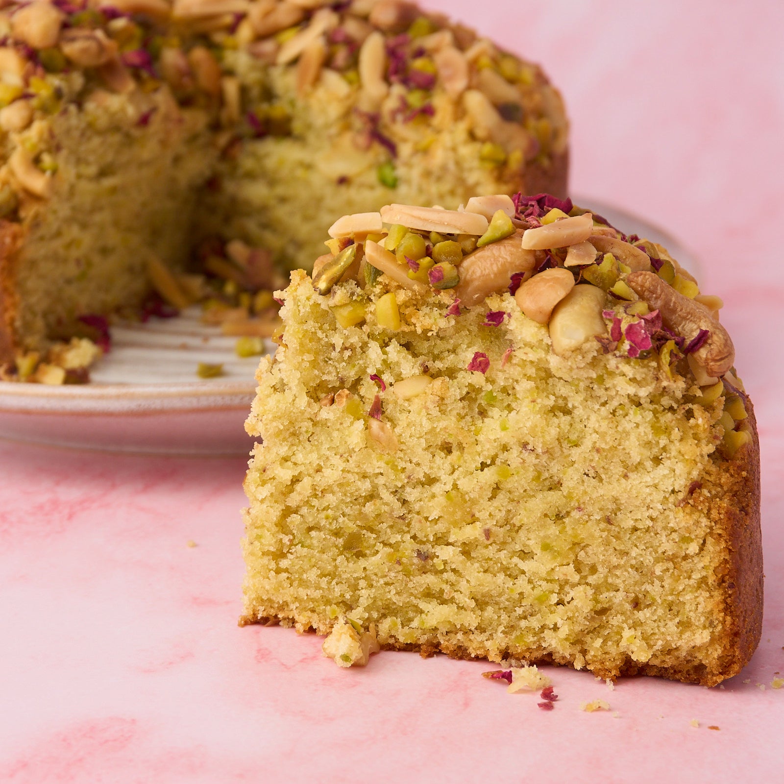 Close-up slice of eggless Pistachio Mawa Cake with pistachio and dry fruit topping