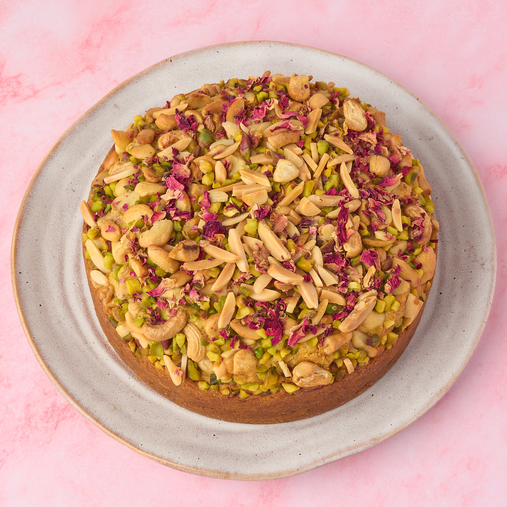 Top view of eggless Pistachio Mawa Cake topped with mixed nuts and rose petals in Sydney