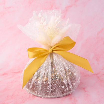 Eggless Pistachio Mawa Cake gift wrapped in decorative net wrap with white floral accent and ribbon by EatWithSimer