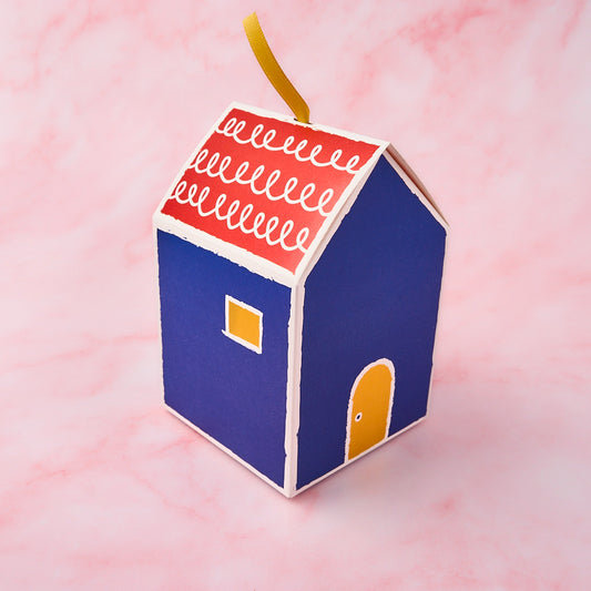 Return gift for housewarming featuring a blue house shaped gift box on a soft pink background